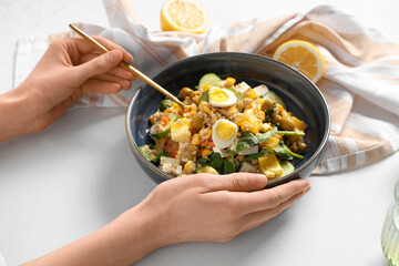Female hands with bowl of healthy quinoa salad on white background, closeup