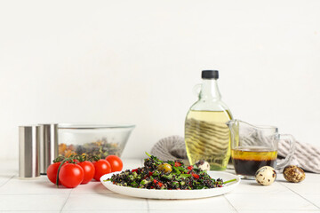 Plate with healthy quinoa salad and ingredients on white tile table near white wall