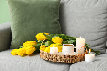 Tray with beautiful candles and cup of coffee on sofa in room, closeup