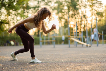 A young woman is exercising with enthusiasm in an urban outdoor park during a beautiful sunset