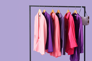 Obraz premium Black rack with stylish clothes and accessories on purple background, closeup