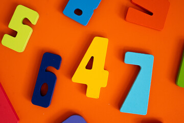 Brightly colored wooden numbers are scattered across an orange surface. The playful digits in yellow, blue, red, green, and light blue evoke fun learning and early math exploration.