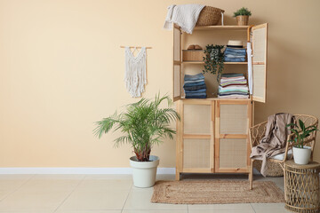 Open wooden closet with clothes and houseplants near beige wall in interior of room