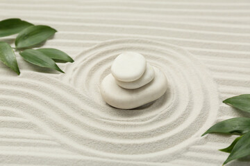 Spa stones, green leaves and lines on sand as background, closeup. Zen concept