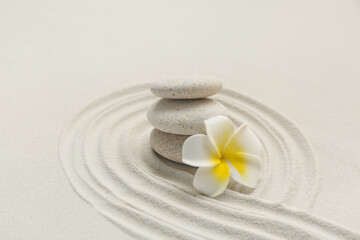 Spa stones and plumeria flower with lines on sand as background, closeup. Zen concept