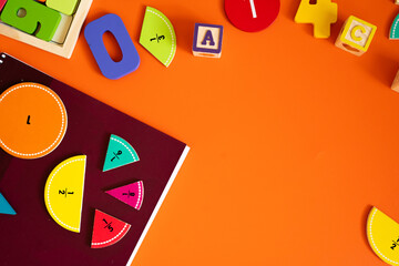 Wooden fraction pieces showing 1, 1/2, 1/6, 1/8, and 1/5 rest on orange background,  yellow letter block, combining math and play in a colorful educational setting.