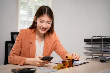 Adult Asian businesswoman manages gold investments smart phone calculating financial growth secure office