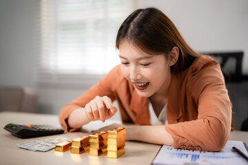 Adult Asian woman happily examining gold bars for wealth management financial investment growth planning strategy secure future on office desk