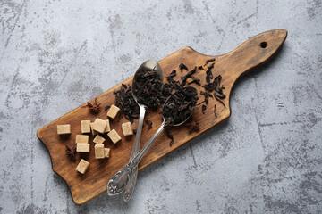 Spoons with dry black tea leaves and cubes of sugar on grey background