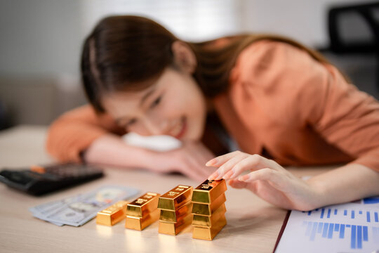 Asian adult woman focus gold bars contemplate investment finance wealth management savings strategy future financial plan success business office desk