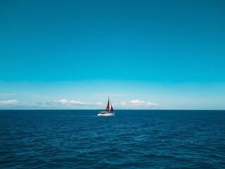 Solitary sailboat navigates vast blue ocean under clear sky