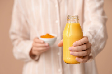 Young woman holding bottle of tasty turmeric drink on beige background, closeup