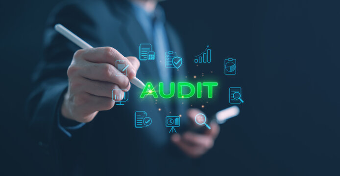 A businessman writing with a digital pen on a virtual screen showing the word AUDIT in green surrounded by glowing blue finance icons, representing business data analysis and corporate audit review.