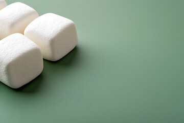 Fluffy marshmallows on a calming green backdrop. These sweet treats evoke cozy feelings and are perfect for roasting or adding to a warm drink. The simple dessert!