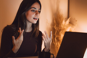 Happy millennial Caucasian woman in earphones sit at desk at home office work distant on computer. Smiling young female in headphones talk speak on webcam online on laptop. Virtual event concept.