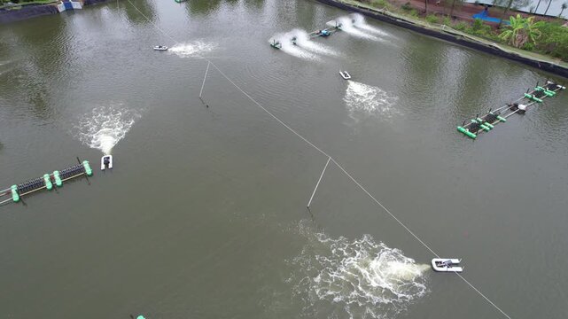 Aerial drone footage of shrimp farming ponds with paddle wheel aerators operating in rural Thailand, aquaculture industry, sustainable seafood production concept.
