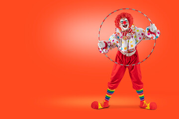 Funny clown looking through hula hoop in the circus, man entertainer as Joker in a suit and wig, with clown whiteface makeup. Trickster, jester, pantomime, mime, and a professional actor at events.