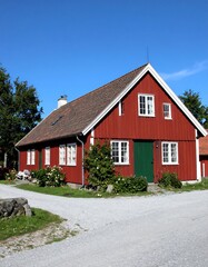 Traditional two-story wooden dwelling, vibrant red exterior, white window frames, green door, gravel driveway, under blue sky
