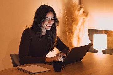 Head shot pleasant happy young woman freelancer working on computer at night. Attractive businesswoman studying online, using laptop software, web surfing information or shopping in internet store.