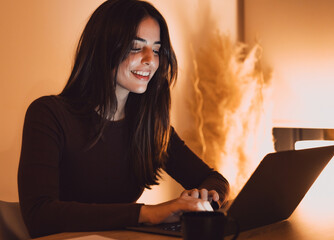 Head shot pleasant happy young woman freelancer working on computer at night. Attractive businesswoman studying online, using laptop software, web surfing information or shopping in internet store.