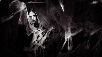 Fototapeta premium gothic woman with creepy vampire makeup trapped in spider web. Fantasy scary girl on halloween background. Black and white photo
