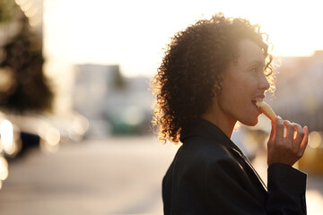 Side profile of a woman with curly hair eating ice cream outdoors in sunset light. Warm golden tones, natural emotion, and large copy space for summer lifestyle advertising.