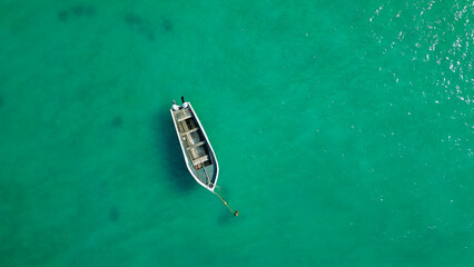 Lonely fishing boat floating above clear teal water overhead composition minimal travel background aesthetic