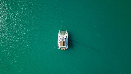 Top down drone view of white sailing catamaran anchored on turquoise lagoon minimal composition calm summer water