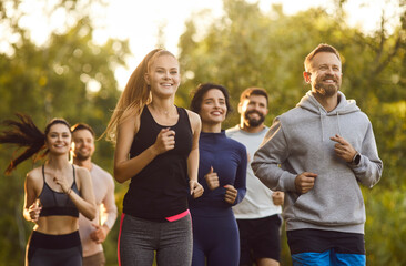 Team of cheerful active young people in sportswear running together in park, having training in nature, enjoying fresh air outdoors, promoting physical fitness, leading healthy lifestyle. 