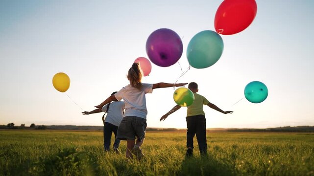 Children running with balloons at sunset children run across green grass in open field holding colorful balloon while sun sets on horizon summer play and joy in warm golden light smile laughter