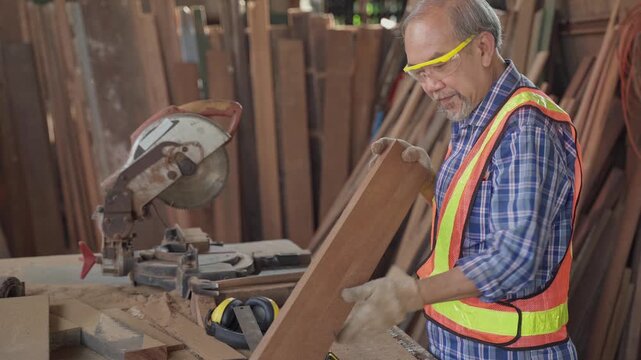 A Carpenter man wearing a mask and a safety vest is cutting wood with a saw. The scene is set in a workshop with many pieces of wood scattered around. The man is focused on his task