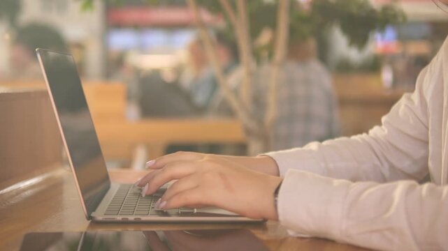 Person is typing on a laptop in a cafe. There are other people in the background. The laptop is open and the person is using it