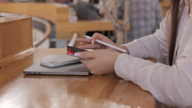 Person is writing on a laptop with a pen. The laptop is on a wooden table. The person is wearing a white shirt