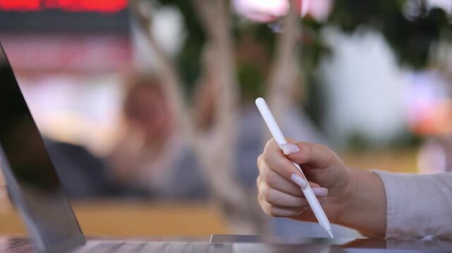 Person is holding a white pen in their hand. The pen is on a laptop. The laptop is on a table