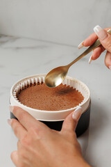 Hand holding spoon over chocolate dessert on marble surface
