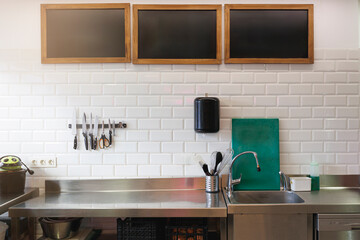 Stainless kitchen counter with utensils on white tile wall