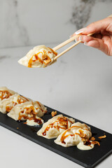 Hand holding dumpling with chopsticks over black plate
