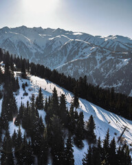 Elevated view of a mountain slope featuring a ski lift and ski runs, set against a backdrop of sweeping, snow-covered mountains