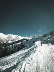 Low angle view of a skier or snowboarder ascending a steep, snow-covered mountain ridge under a bright blue sky