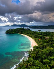 Tropical bay with white sand beach, dense jungle, and dramatic clouds