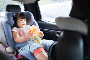 The little girl was so cute drinking water while sitting in the back seat of his car during his trip,Little girl sitting in car seat and drinking water during long journey.