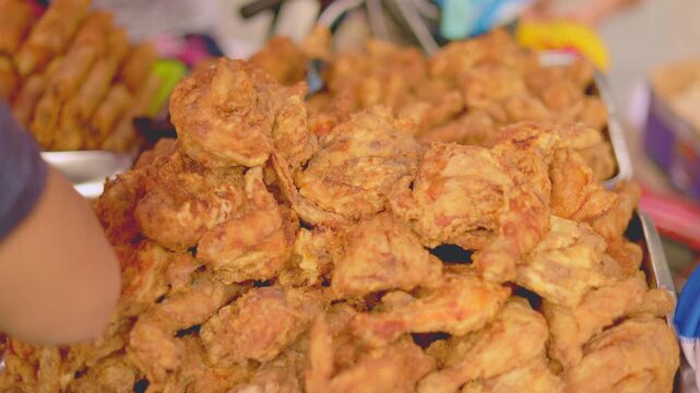 Crispy chicken vendor arrangement, closeup of crispy chicken with vibrant market background and customers, vendor arranging crispy fried chicken in busy market with colorful packaging and warm