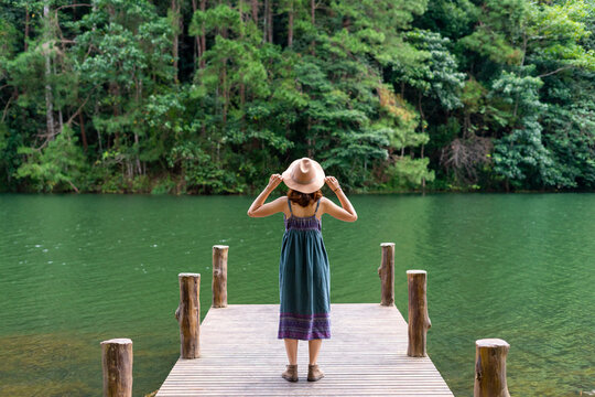 Young asian woman traveler with backpack holding hat and looking at amazing mountains in the forest. Relax time on holiday of hipster style. Nature travel concept.