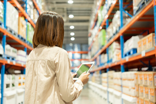 Warehouse worker hands holding tablet check stock on tall shelves in warehouse storage. Asian woman auditor or staff work looking up stock taking inventory in cargo store. Owner start up business.