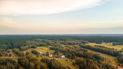 Fototapeta premium Aerial view of serene green landscape with fields and scattered houses under a soft evening light. Ideal for themes of nature, rural living, and tranquility.