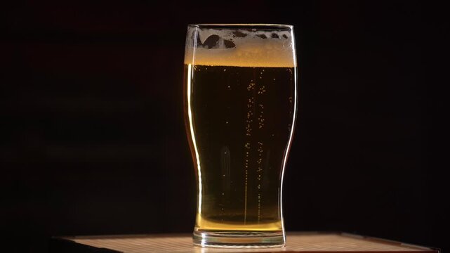 Fresh beer in a glass with bubbles on black background, close-up. Alcohol drink on a bar counter.