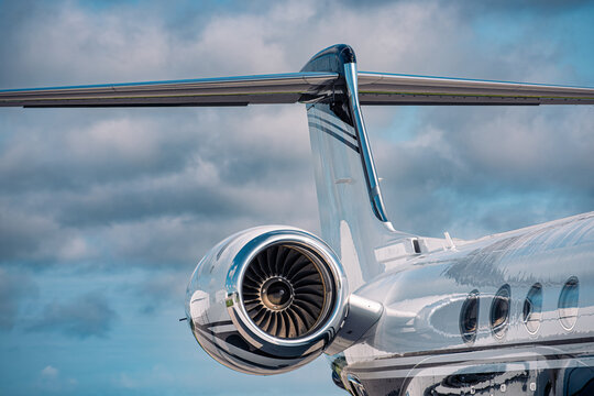 Close-up of a polished jet engine and T-tail on a modern business jet, reflecting the cloudy sky above the airport.