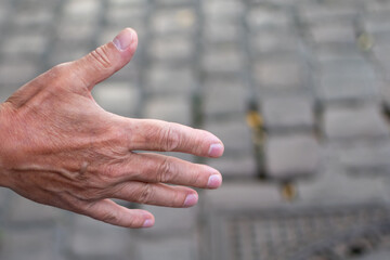 Close-up photo of a person's outstretched open hand, showing skin texture and veins, with a blurred background of grey cobblestones or pavement