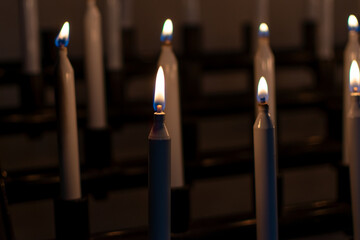 Low-light photo of several tall, white votive candles burning brightly in a church or sanctuary, creating a solemn and peaceful atmosphere