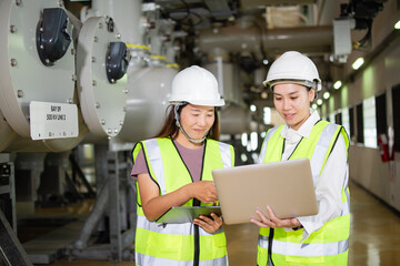 Working together at a high voltage electrical substation, two female engineers use a laptop to inspect, monitor, and analyze power system performance, ensuring safety and efficiency in energy 